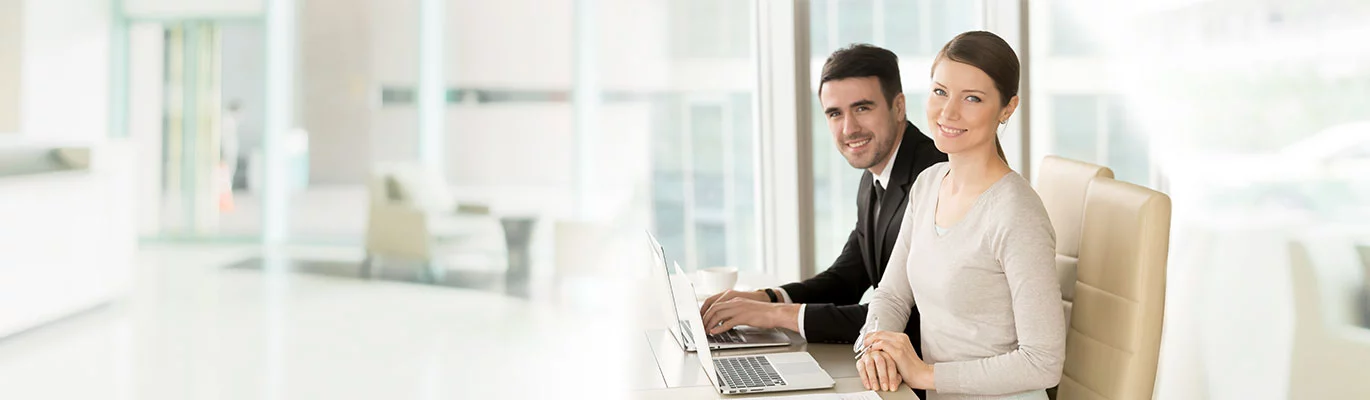 Two Network professionals can be seen sitting adjacent to each other with their laptops on table.